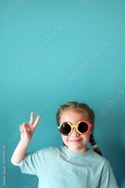 Fototapeta Cheerful girl 6-8 years old on a emerald color background with a gradient spot for text - vertical banner