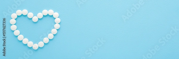 Fototapeta Heart shape created from white pills on light blue table background. Pastel color. Closeup. Healthcare concept. Wide banner. Empty place for text. Top down view.