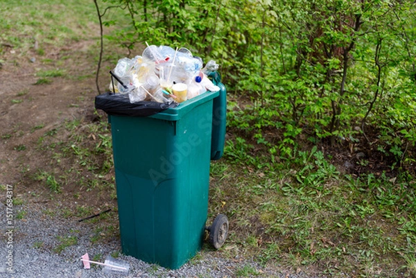 Obraz The garbage container on wheels is completely filled with garbage.