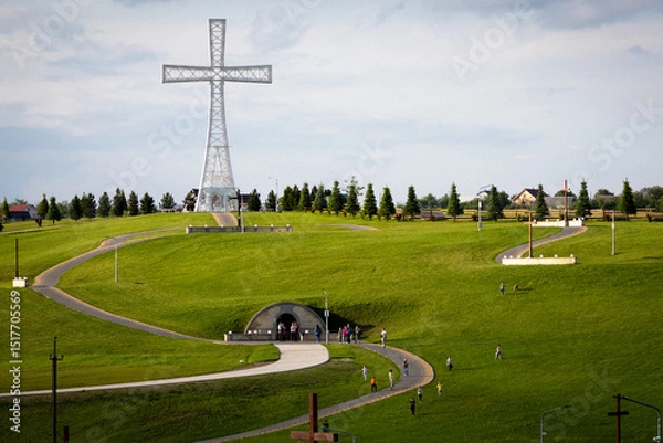 Fototapeta People climb the gently curved path up the hill towards the towering cross, passing stations of the cross and smaller wooden crosses on the way