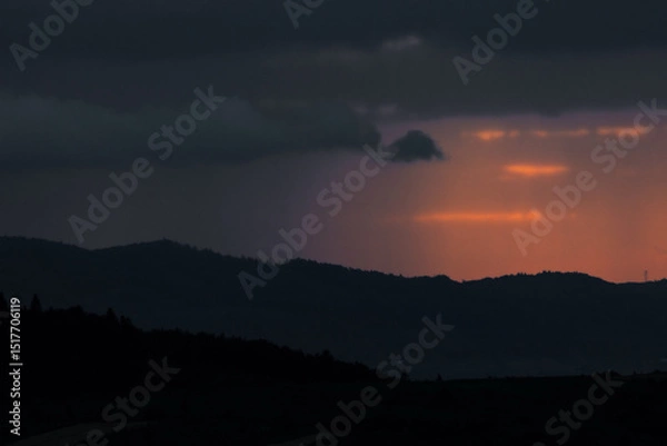 Fototapeta Evening mist rolls over the mountain ridges as clouds catch the last golden rays of sunlight. A surreal, cinematic view perfect for travel or weather-themed content