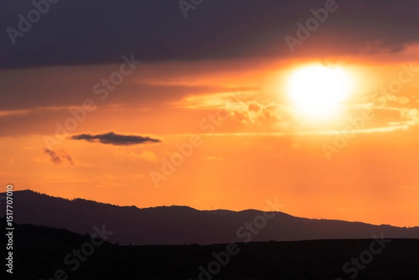 Fototapeta Golden hour sunlight illuminates the silhouette of distant mountains under glowing clouds