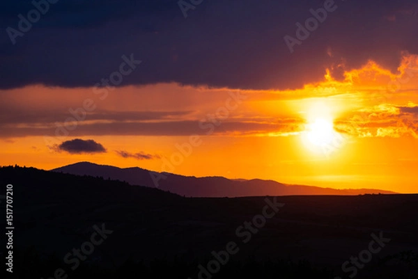 Fototapeta Sunbeam breaks through clouds at twilight above a mountain horizon in vivid tones