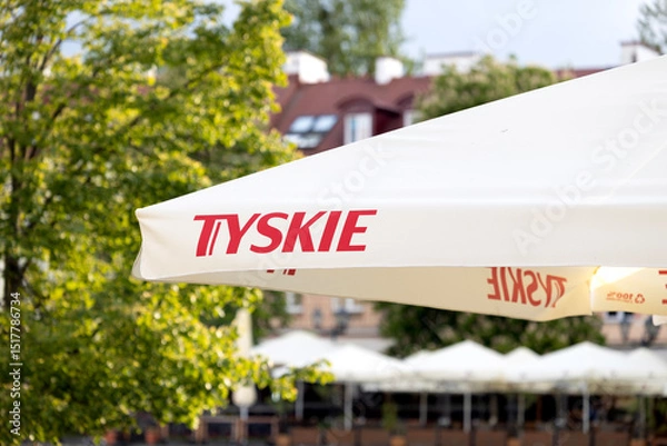 Fototapeta Bialystok,Poland -May 19,2025 Tyskie branded white patio umbrella in an outdoor area with trees and buildings in background