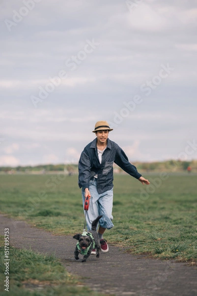 Obraz Teenager girl running with dog in a park during a cloudy day