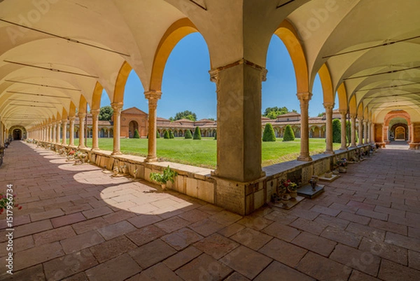 Fototapeta Ferrara, Italy - May 17, 2025: Wide angle view of the Charterhouse of Ferrara's cloister, featuring columns, arches, a green lawn, and a blue sky
