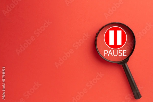 Fototapeta Magnifying glass focusing on a red pause button icon with white bars and 'PAUSE' text.Concept of taking a break,stopping for reflection, work hiatus,analyzing an interruption,or media player control.
