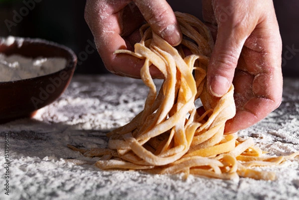 Obraz Caucasian female hands holding raw fettuccine noodles after drying