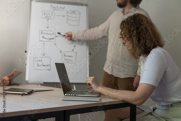 Obraz Three software developers brainstorming in a modern office. Team coding session with laptops showing code, planning web development and design. Tech startup environment and teamwork