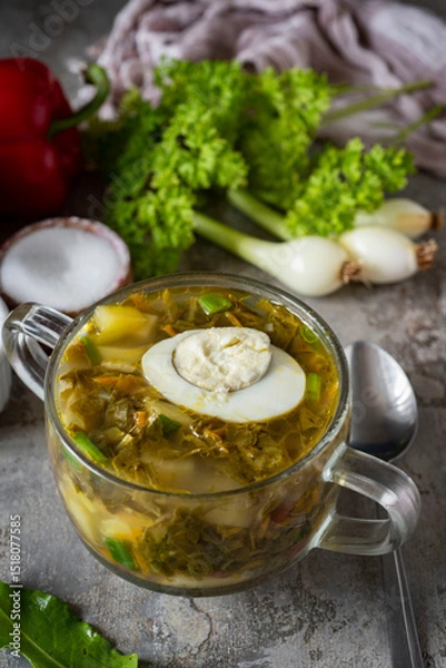 Fototapeta Hearty dinner: soup with sorrel and egg in a transparent plate close-up. Hot soup with sorrel for lunch. Close-up. Vertical photo