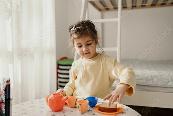 Fototapeta Happy Little Girl Playing with Toy Tea Set at Home. Pretend Tea Party Playtime with Colorful Toy Set in Cozy Bedroom