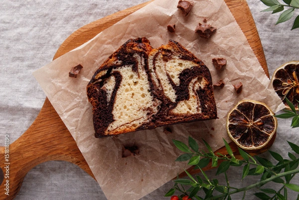 Fototapeta slice of marble cake with chocolate swirl on parchment paper, rustic dessert, wooden background