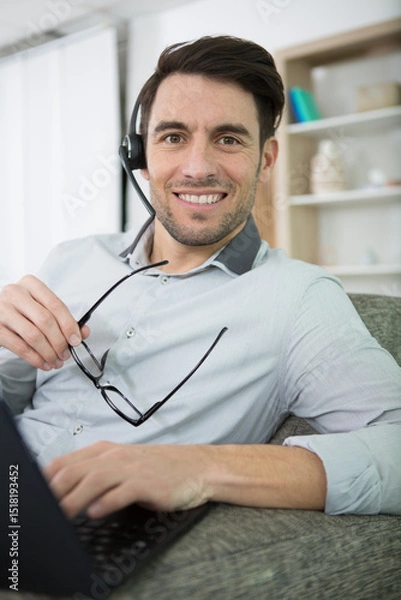 Fototapeta suave man sat on sofa using headset and laptop computer