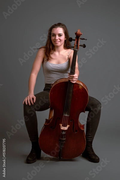 Fototapeta Young female cellist posing with her instrument on gray background