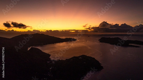 Fototapeta A fiery sunset bathes the horizon in warm light, while the islands and water rest in shadows. Praslin, Seychelles.
