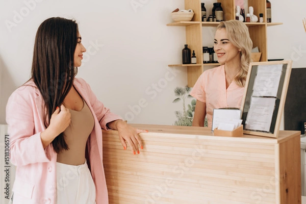 Fototapeta Young uniformed spa receptionist warmly greeting a female client at a modern spa reception