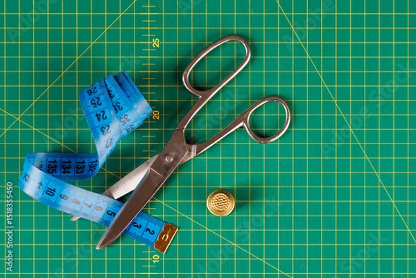 Fototapeta Close-up of Sewing Tools: Measuring Tape, Scissors, and Thimble with Cutting Mat in the Background. View from above.
