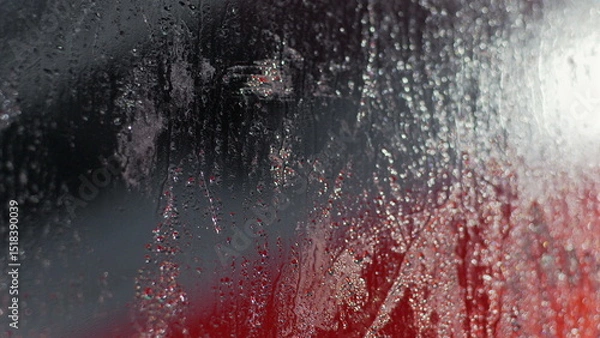 Fototapeta Raindrops and condensation creating a sparkling effect on glass, red and dark background visible through streaks and droplets, abstract scene with water patterns and reflections
