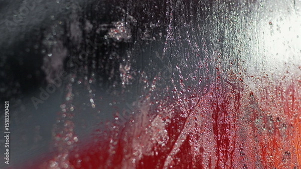 Fototapeta Raindrops and condensation creating a sparkling effect on glass, red and dark background visible through streaks and droplets, abstract scene with water patterns and reflections