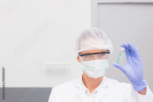 Fototapeta Scientist holding small transparent vial with pale green liquid in laboratory by grey cabinet