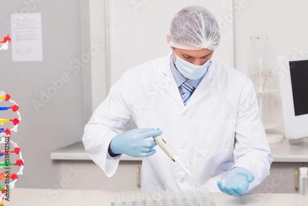 Fototapeta Scientist pipetting samples into multi-well plate near DNA model and computer monitor at lab bench