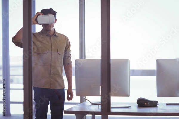 Fototapeta Man wearing VR headset interacting near glass partition in modern office with dual monitors