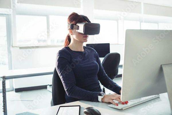 Fototapeta Virtual reality headset resting on white desk near monitor and tablet under natural light in office