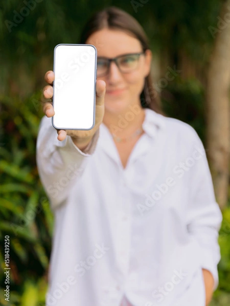 Fototapeta Smiling woman showing smartphone with blank screen outdoor. Mockup for app, website, or social media design.