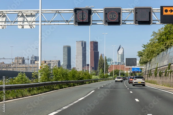 Obraz Urban highway A12 entering The Hague, Netherlands, with modern skyscrapers in the background and cars driving under digital speed limit signs.