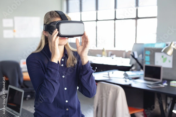 Fototapeta Virtual reality headset sitting on desk among monitors laptops papers in bright open office