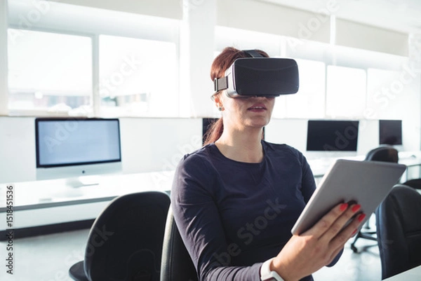 Fototapeta Virtual reality headset and tablet resting on black swivel chair in bright computer lab, copy space