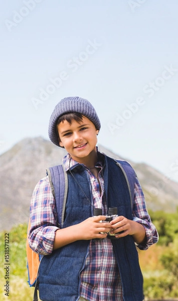 Fototapeta Middle Eastern boy standing on mountain path holding binoculars and wearing orange backpack