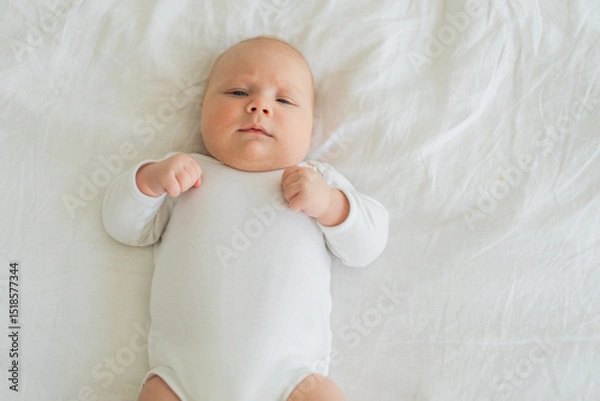 Fototapeta Happy baby. Cute little newborn girl with smiling face lying on bed in bedroom. Infant baby resting playing lying down on white blanket at home. Motherhood happy child childcare concept