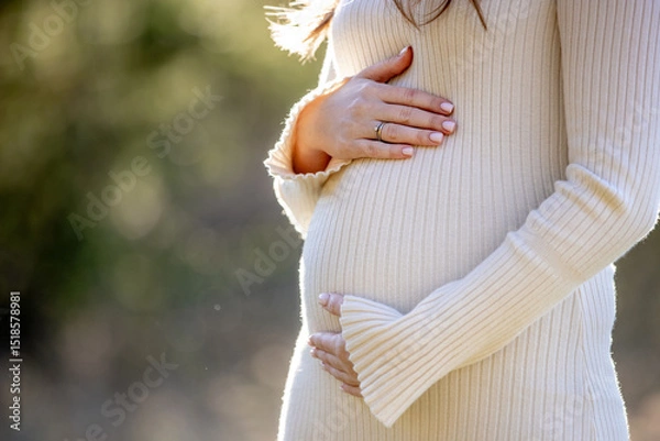 Fototapeta A beautiful pregnant woman is posing gracefully amidst a lush green setting, radiating immense joy and tranquility
