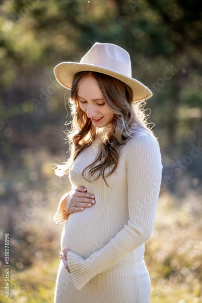 Fototapeta A beautiful pregnant woman is posing gracefully amidst a lush green setting, radiating immense joy and tranquility