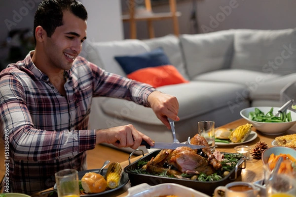 Fototapeta Man carving roast turkey at wooden dining table with carving knife and meat fork, copy space