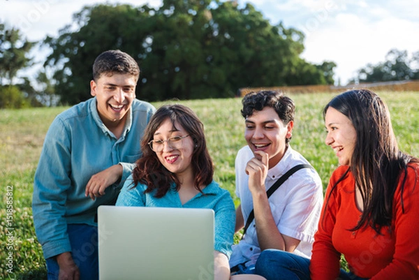 Fototapeta Group of students watching laptop and smiling together in park