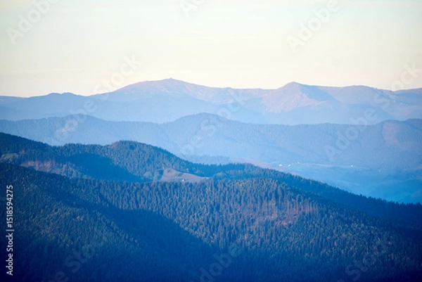 Fototapeta Serene view of rolling mountains in shades of blue and green, with distant peaks under soft, pastel sky, creating peaceful and tranquil landscape.