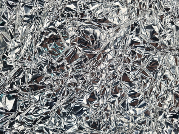 Fototapeta Crinkled silver metallic surface, creating an abstract texture with intricate folds and reflections. The shiny wrinkles form a chaotic pattern, enhancing light interplay and shimmering appeal