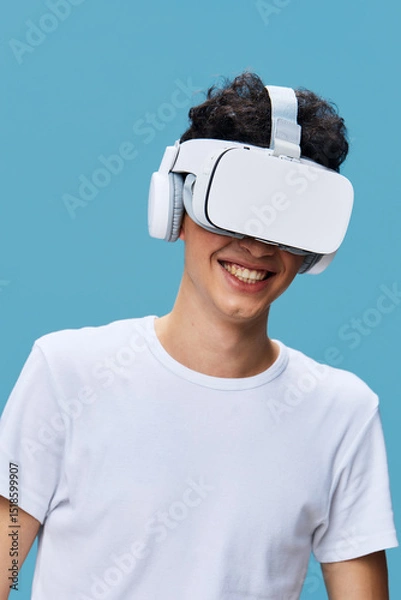 Fototapeta young man wearing virtual reality headset smiling with excitement against blue background, casual white t-shirt, technology and innovation concept, immersive experience