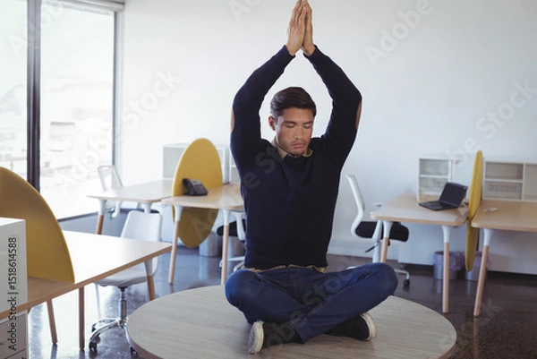 Obraz Pacific Islander man wearing navy sweater meditating on round table in open-plan office with laptop