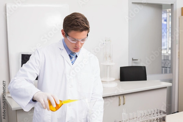 Fototapeta Erlenmeyer flask pouring bright yellow solution through glass funnel into beaker on white lab bench