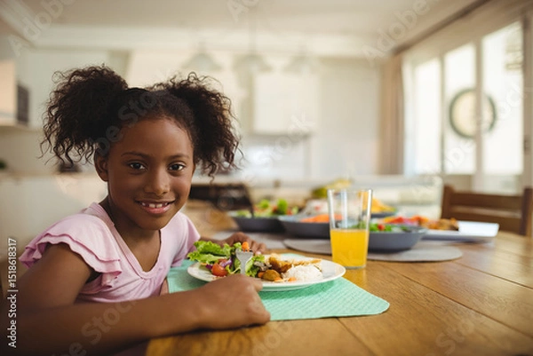 Obraz Child is eating salad, rice, chicken on mint green placemat at wood table in modern kitchen