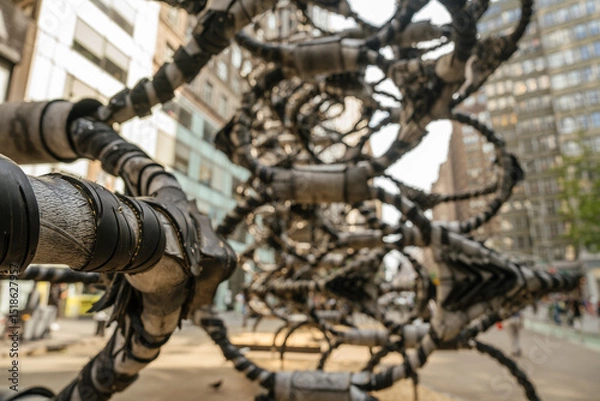 Obraz A close-up of an intricate metal sculpture in an urban setting. The background reveals modern buildings and city life.
