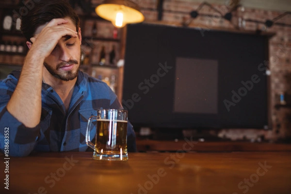 Fototapeta Glass mug of beer resting on bar counter beneath glowing pendant lamp against exposed brick wall
