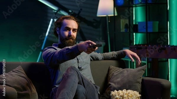 Obraz Man taking seat on sofa to watch television, getting entertained in relaxed home environment. Person arriving in apartment sitting down on couch to enjoy movies, turning on TV, eats popcorn, camera A