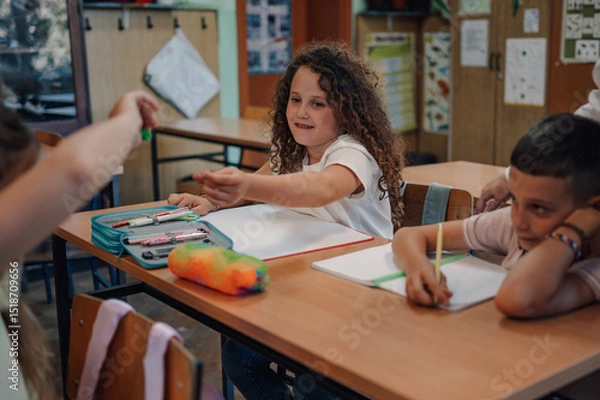 Fototapeta Girl passing a pen to classmate during class at elementary school