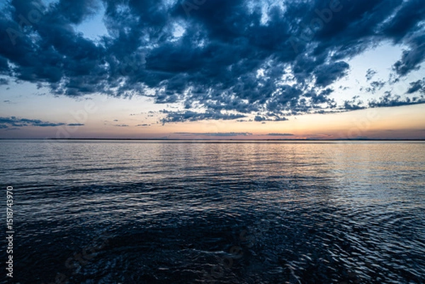 Obraz Tranquil sunset over Lake Saint-Louis in Quebec with dramatic clouds and calm water reflecting the fading light. Peaceful nature moment captured at dusk.