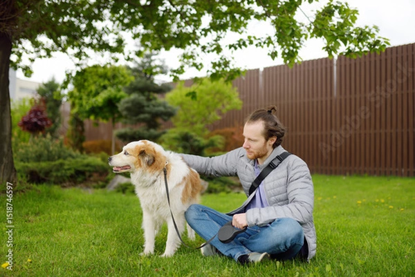 Fototapeta Young man owner walking with his large dog in public park on spring day. Pet care