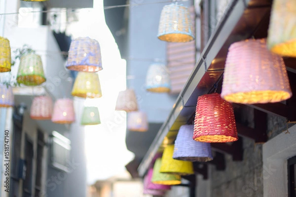 Fototapeta Decorative multicolor wicker lamps are hanging under the street in a small European town